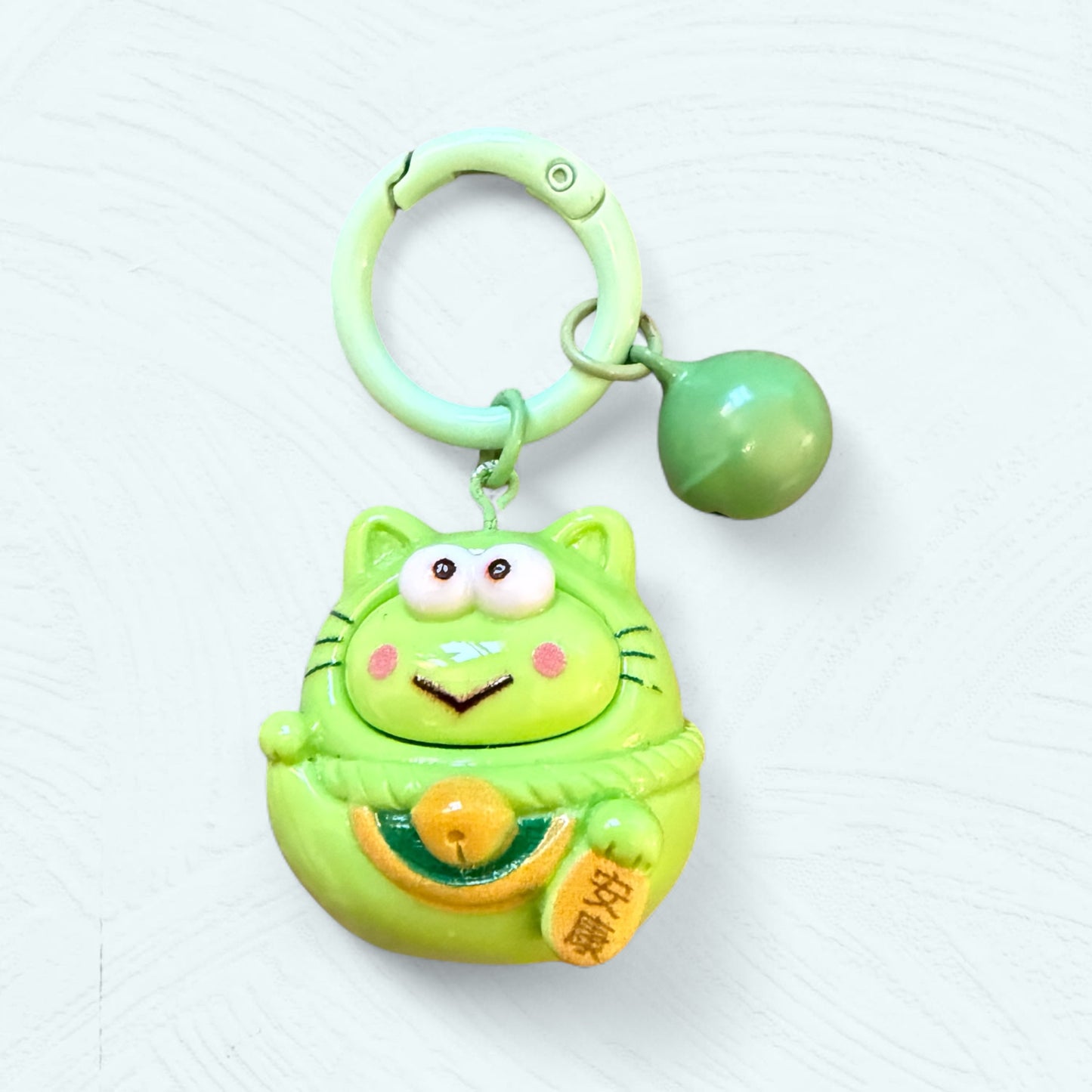 Porte-clés Daruma Keroppi, en vert vif avec de grands yeux ronds et un sourire malicieux.