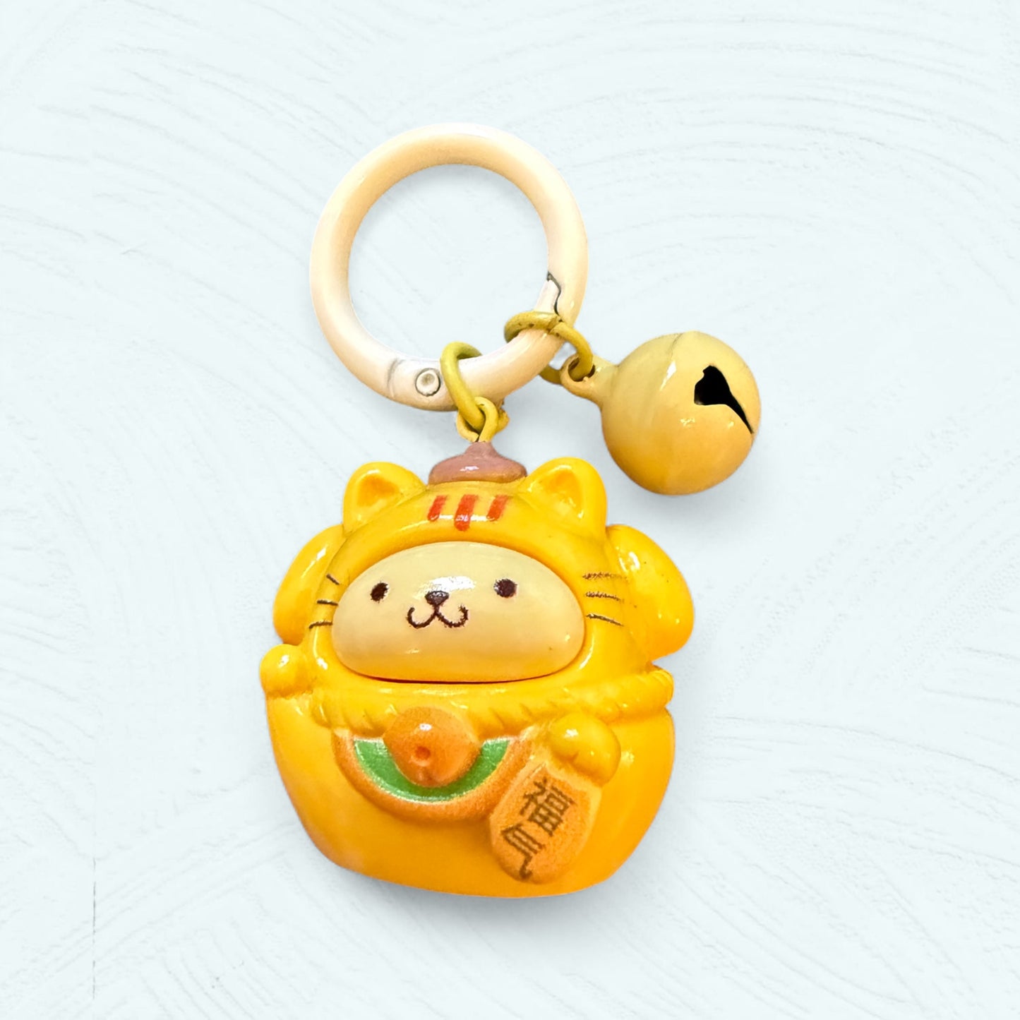 Porte-clés Daruma Pompompurin, jaune et dodu avec un petit béret marron sur la tête.