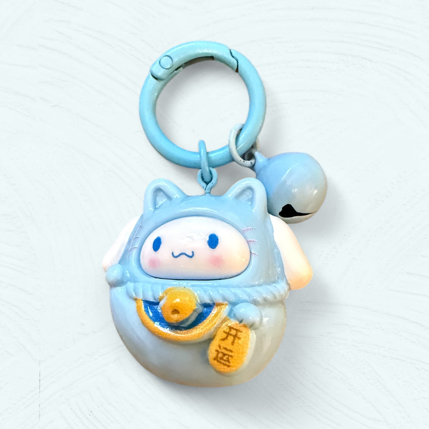Porte-clés Daruma Cinnamoroll, en bleu clair avec de grandes oreilles repliées et un visage souriant.