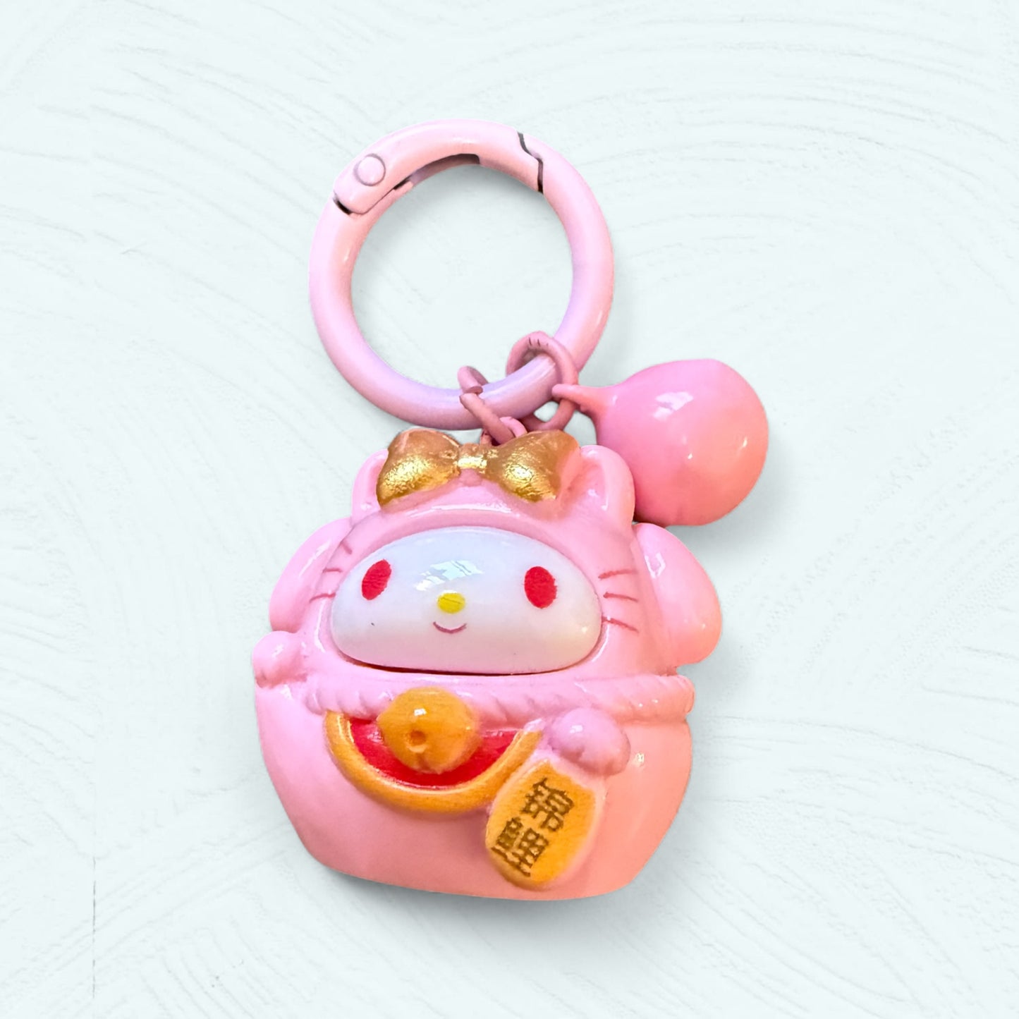 Porte-clés Daruma My Melody, en rose avec des oreilles couvertes et un nœud, expression douce et mignonne.