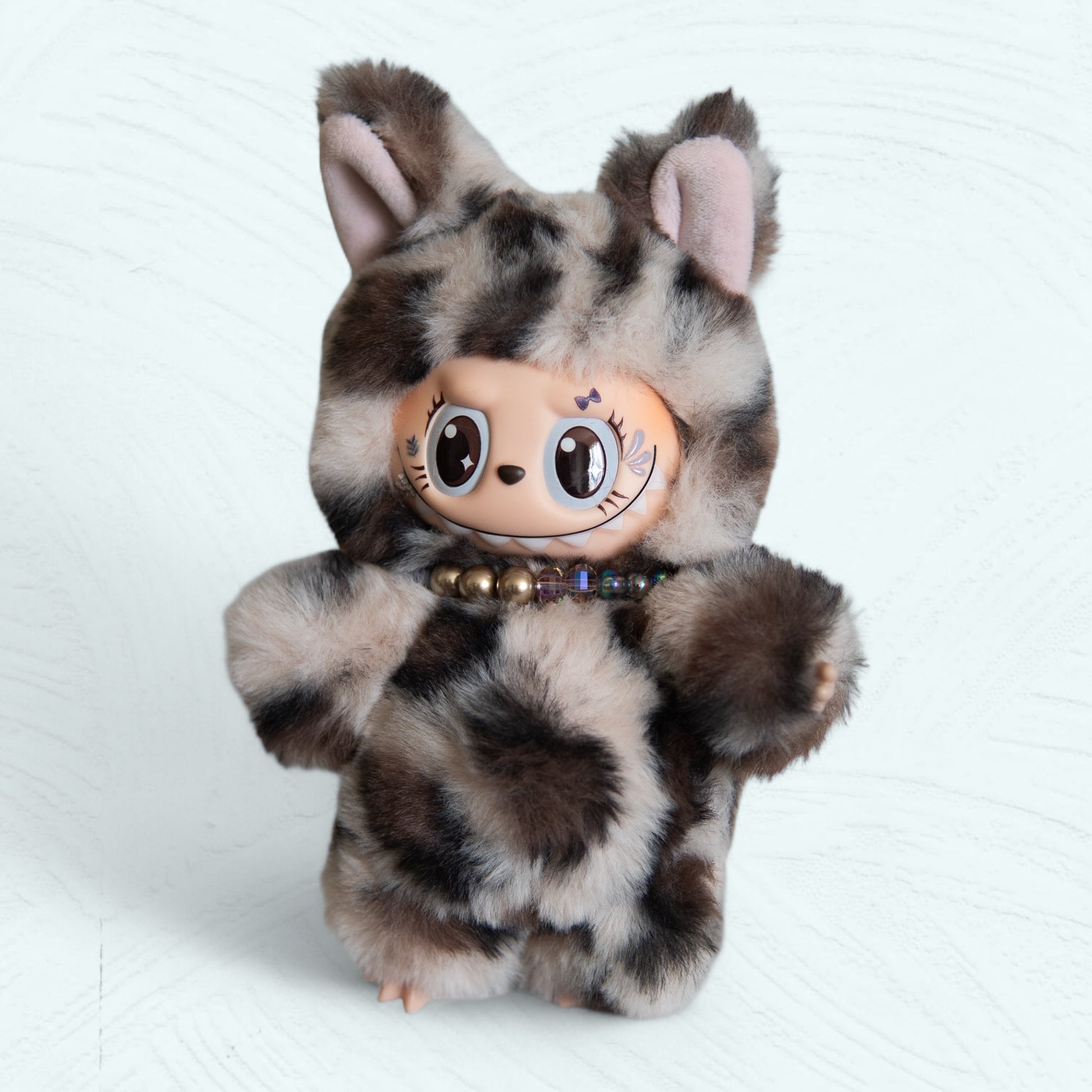Labubu en costume de léopard vu de face, peluche tachetée et collier de perles.