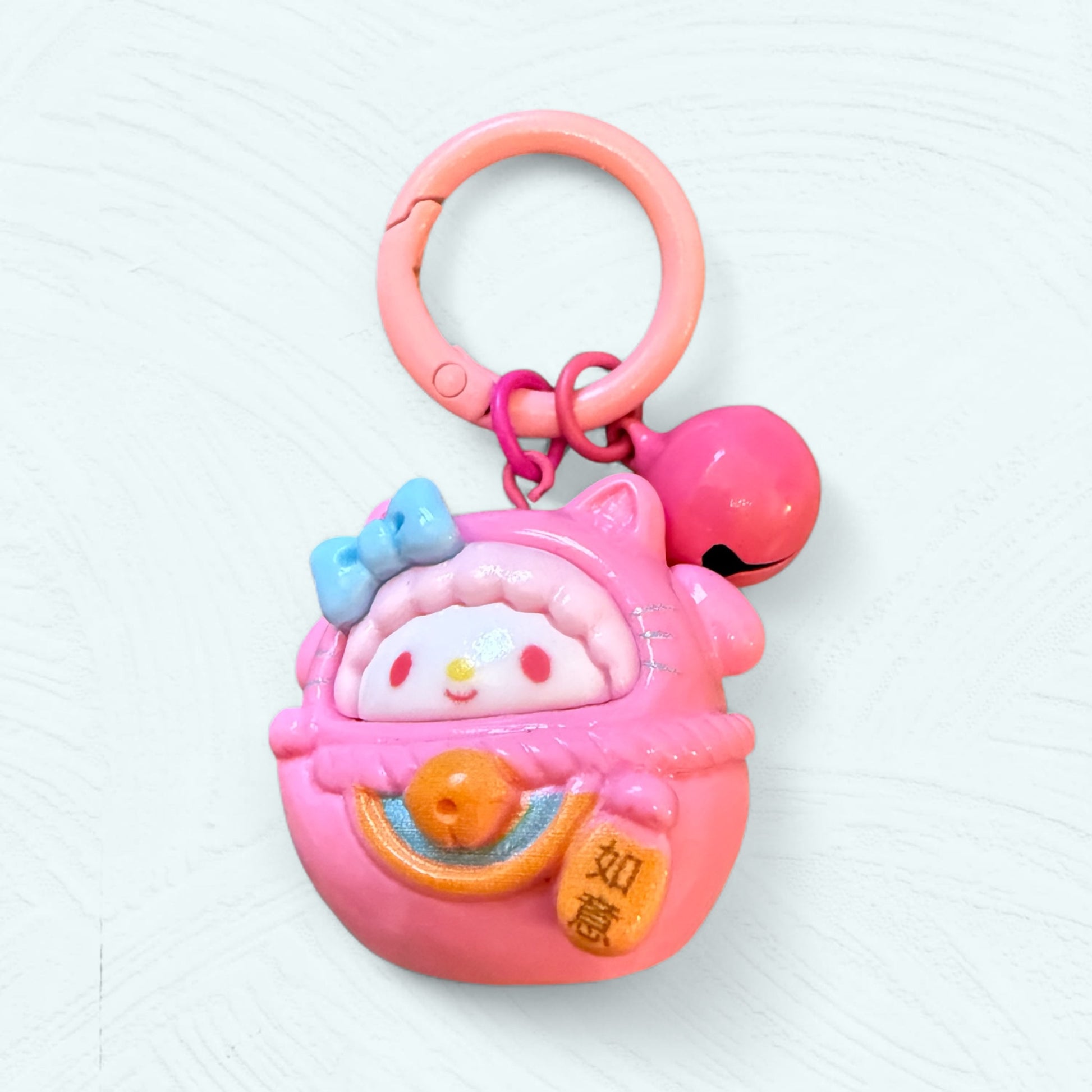 Porte-clés Daruma Piano, en rose bonbon avec un nœud bleu, expression douce et oreilles de chat.